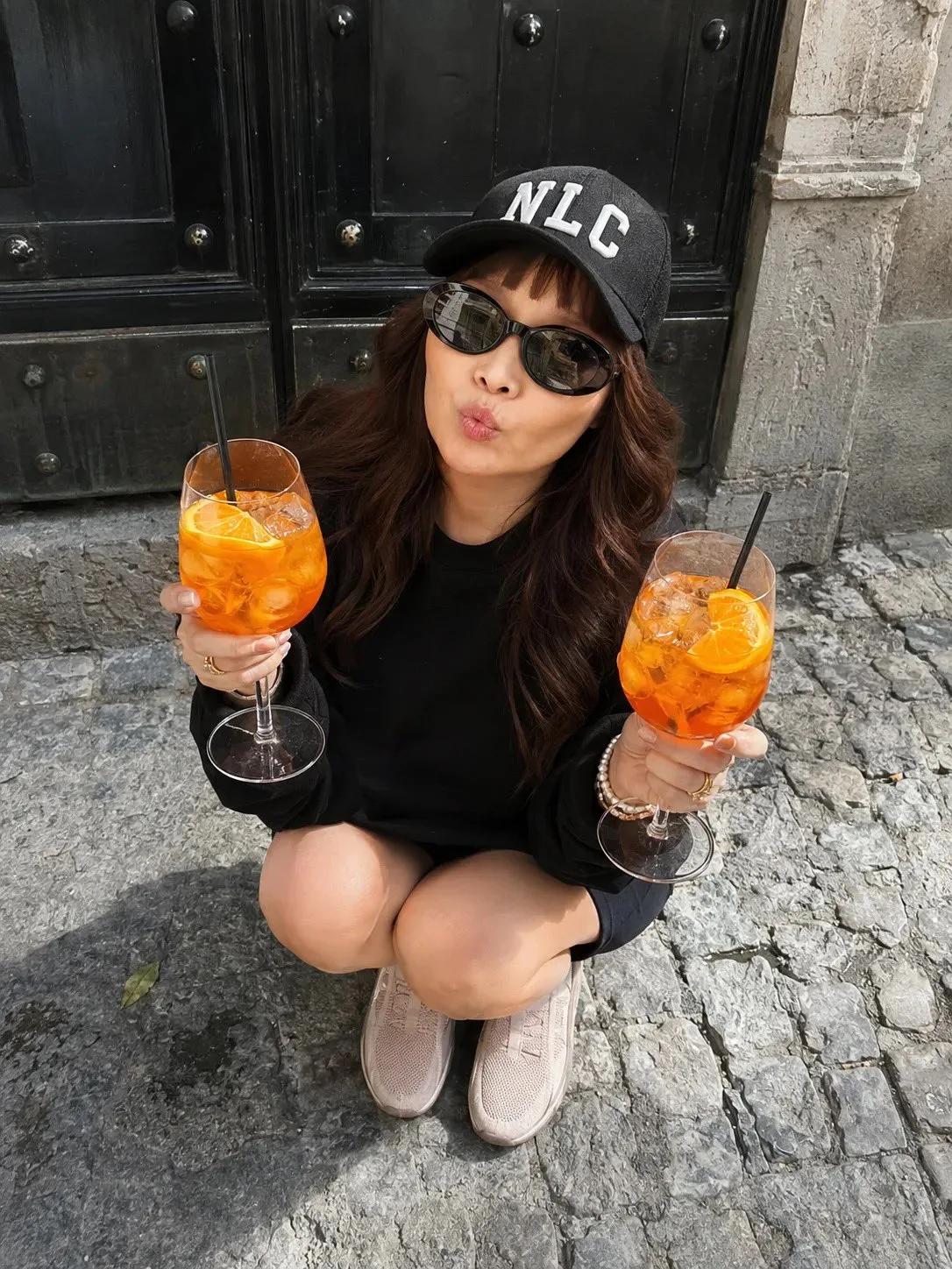 Playful Crouching Pose by a Black Door with Orange Drinks - Image prompt preview