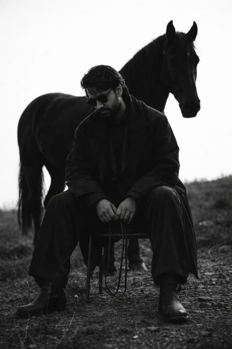 A bearded man with dark wavy hair wearing dark sunglasses, dressed in a l...