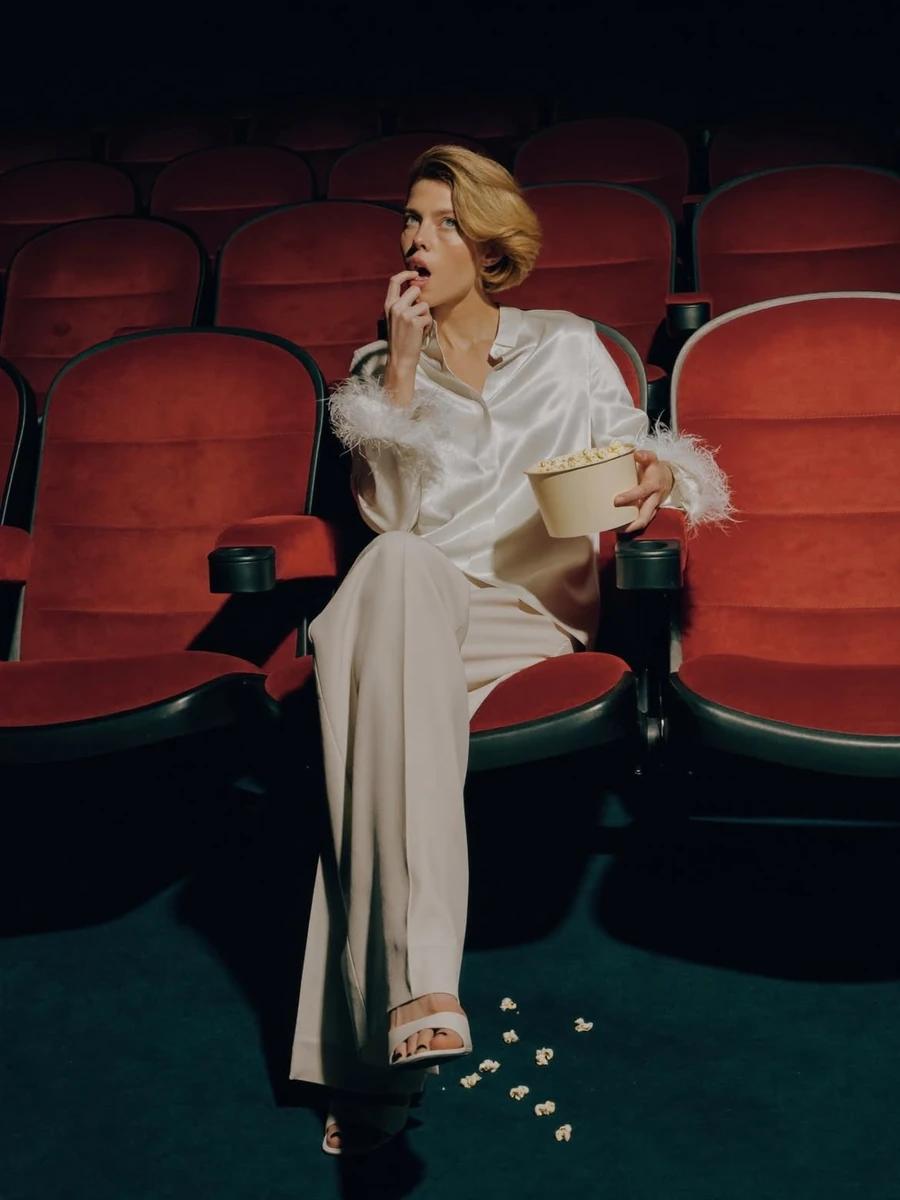 Elegant fashion editorial of a stylish woman sitting alone in a dark movi...